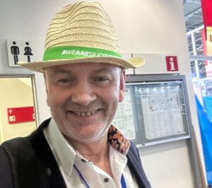 A man smiling at the camera, wearing a straw hat